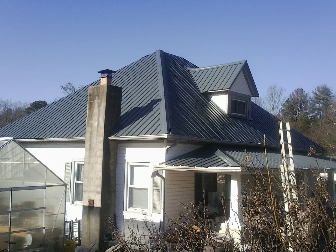 Dark blue standing seam metal roof on a white farmhouse with dormer — Slate & Tile Roof Repair by Roofing Brothers in Montauk