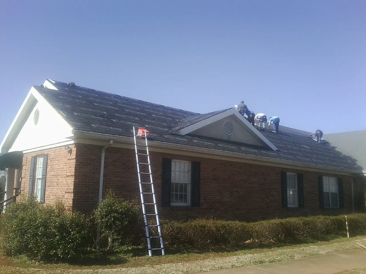 Crew tearing shingles off a brick ranch roof with a ladder set — Emergency Roof Repair work by our crew in Montauk