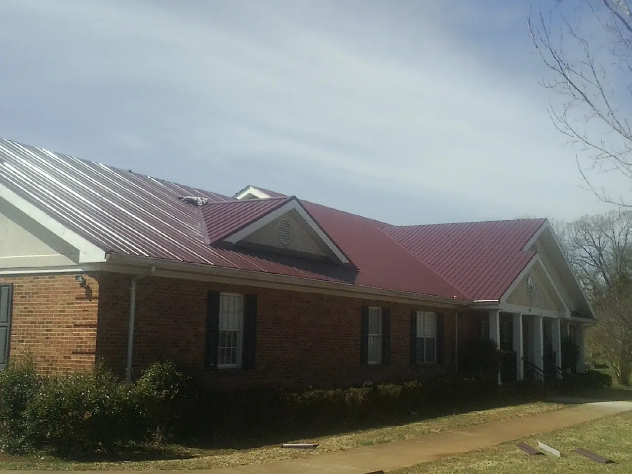 Red metal roof with gabled entries on a long brick building, from a Hail Damage Roof Repair job in Montauk