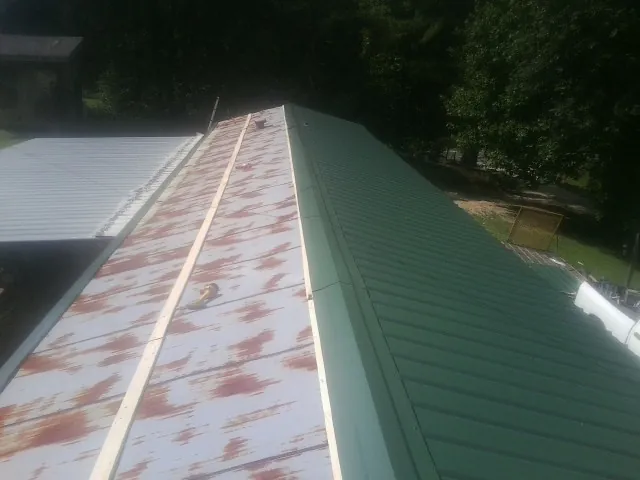 Old rusted panels beside newly installed green metal roofing — Wind Damage Roof Repair by Roofing Brothers in Montauk
