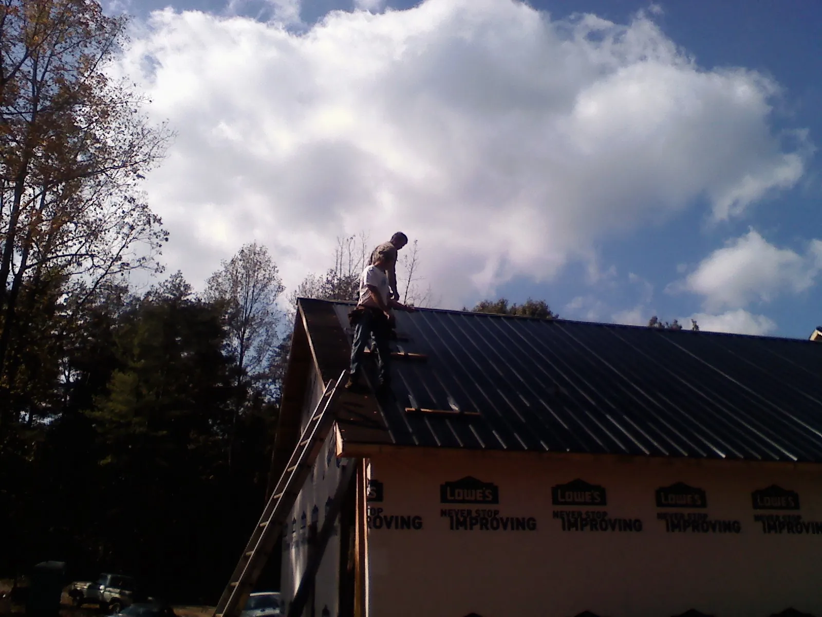 Roofer fastening dark metal panels high against a cloudy sky, from a Roof Inspection job in Montauk