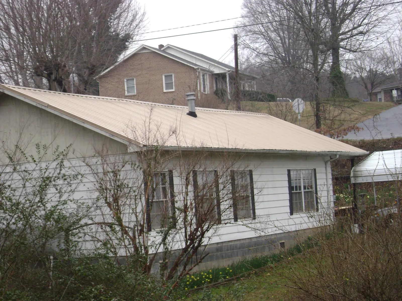 Tan metal roof on a white sided house set into a hillside — Commercial Roofing by Roofing Brothers in Montauk